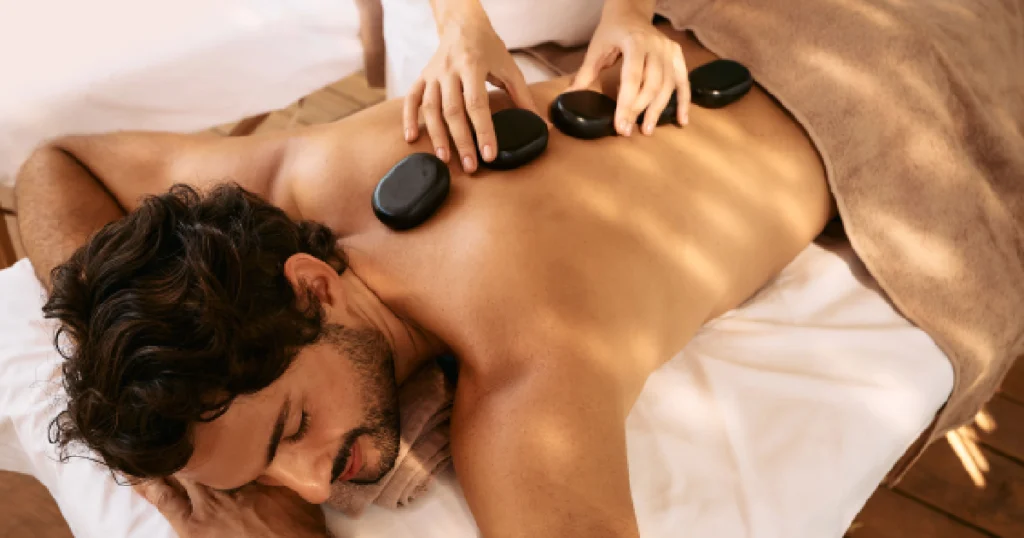 A man lies face-down while a therapist giving hot stones massage in South Ogden, UT